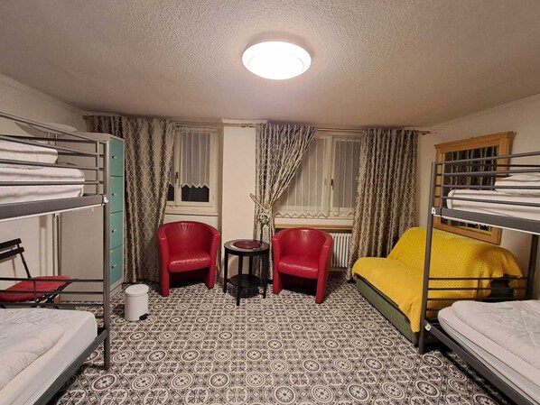Una habitación compacta con literas, una mesita, dos sillas rojas y un ventanal con cortinas.