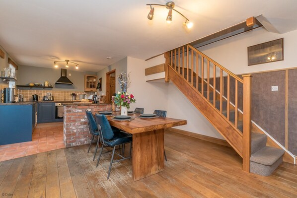 A spacious kitchen with a central island, a dining area with a wooden table, and a staircase with a glass railing.