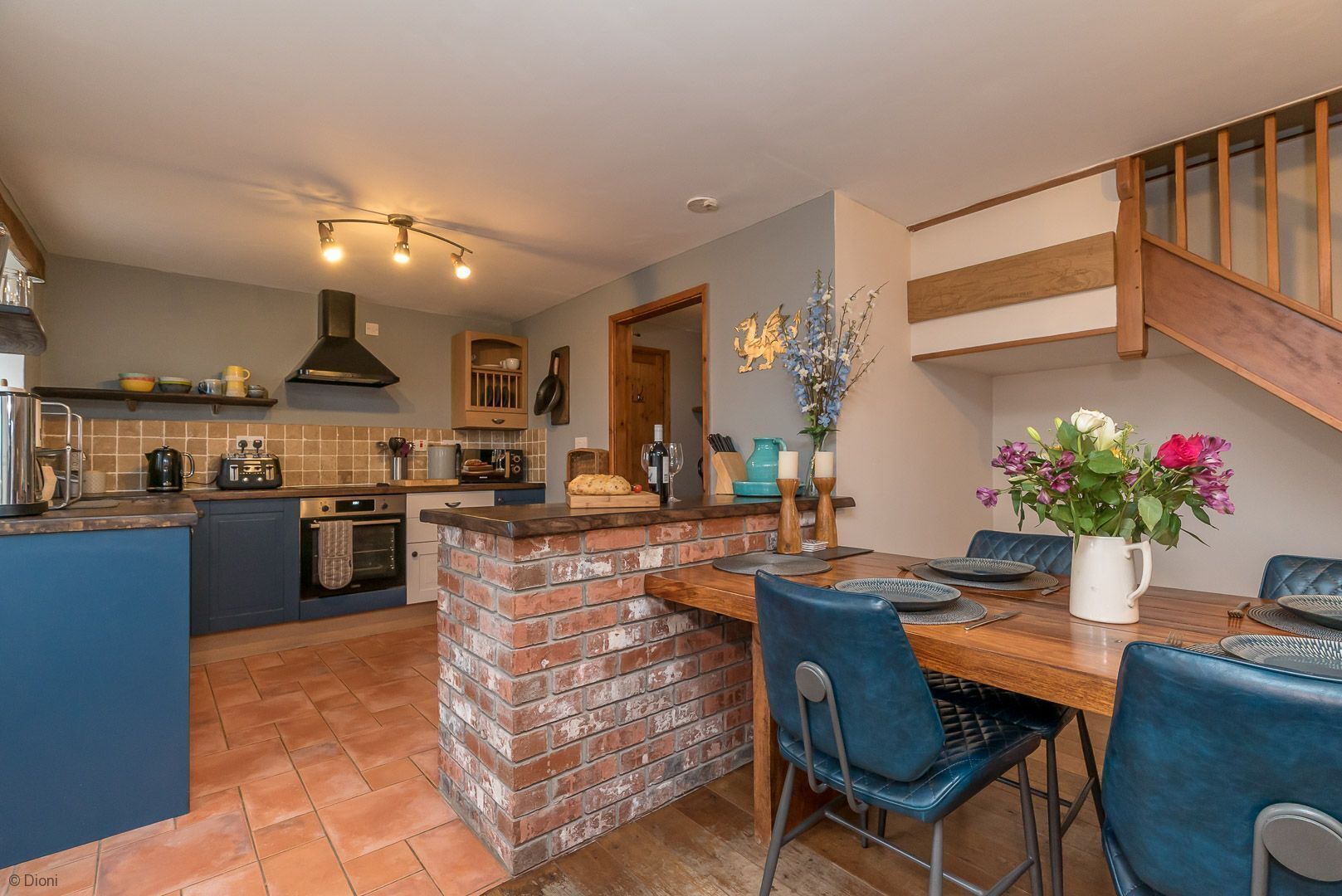 A modern kitchen with a brick island, blue chairs, and a dining table set for six.
