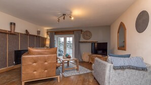 Ein Wohnzimmer mit Ledersessel, grauem Sofa, Couchtisch aus Holz und Flachbildfernseher.