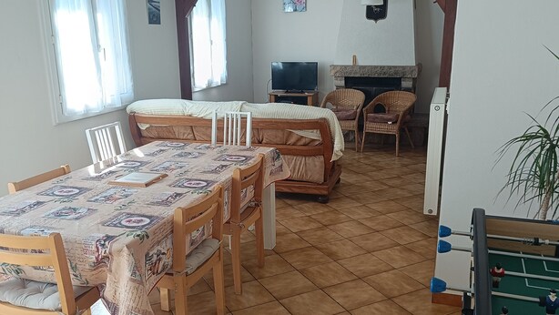 Ein Essbereich mit einem für sechs Personen gedeckten Tisch, einem Tischfußballtisch und einem Fernseher im Hintergrund.