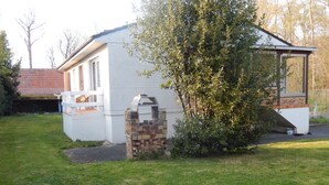 Ein Haus mit Grillplatz aus Ziegelsteinen, heller Fassade und Baum im Vorgarten.