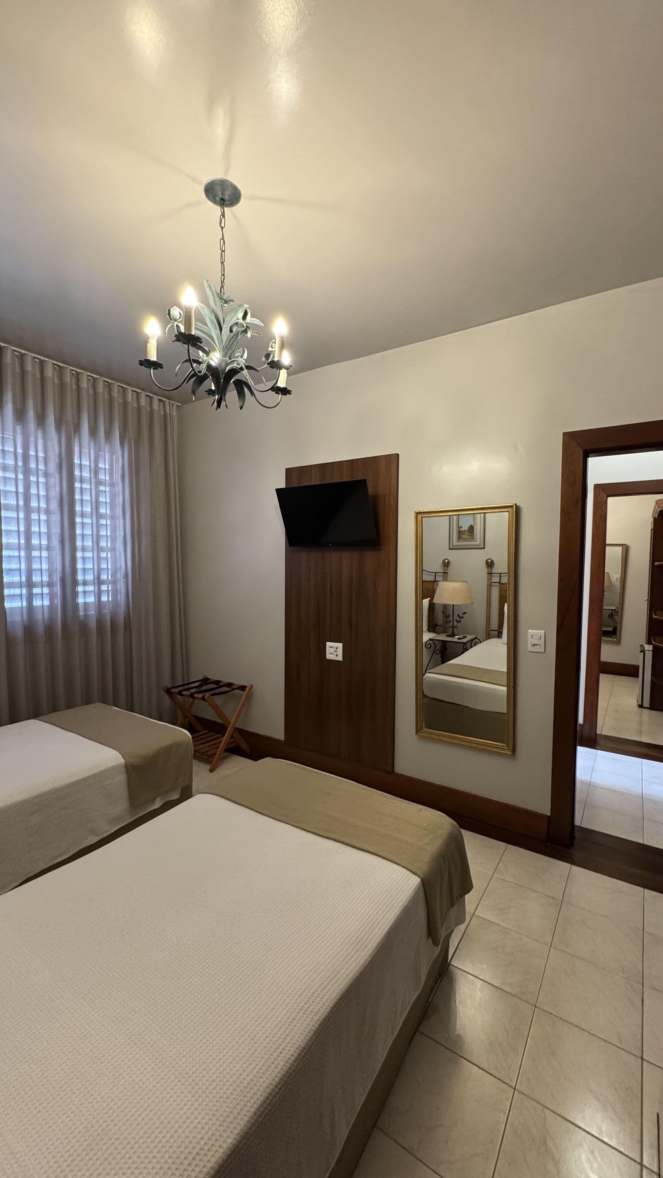 A hotel room with two beds, a television, a mirror, and a chandelier.