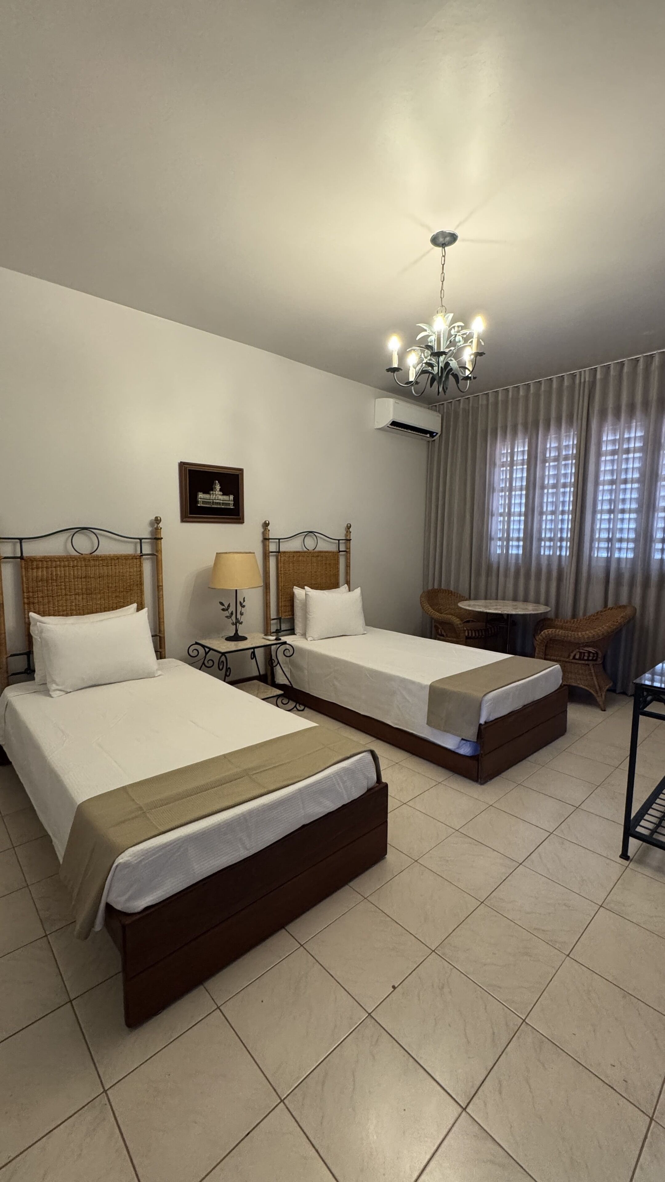 Habitación de hotel con dos camas, un candelabro, un equipo de aire acondicionado, una mesita y una silla.