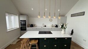A modern kitchen with a central island, pendant lights, and a clock on the wall. - Bader House (Ipswich)