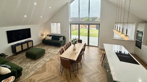 A spacious living area with a high ceiling, a dining table, a sofa, and a kitchen with a large window. - Bader House (Ipswich)