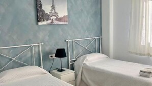 Ett hotellrum med två sängar, ett nattduksbord, en lampa, en tavla som föreställer Eiffeltornet och ett fönster med gardiner.