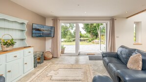 En moderne stue med sofa, fjernsyn og udsigt til det fri gennem en glasdør.
