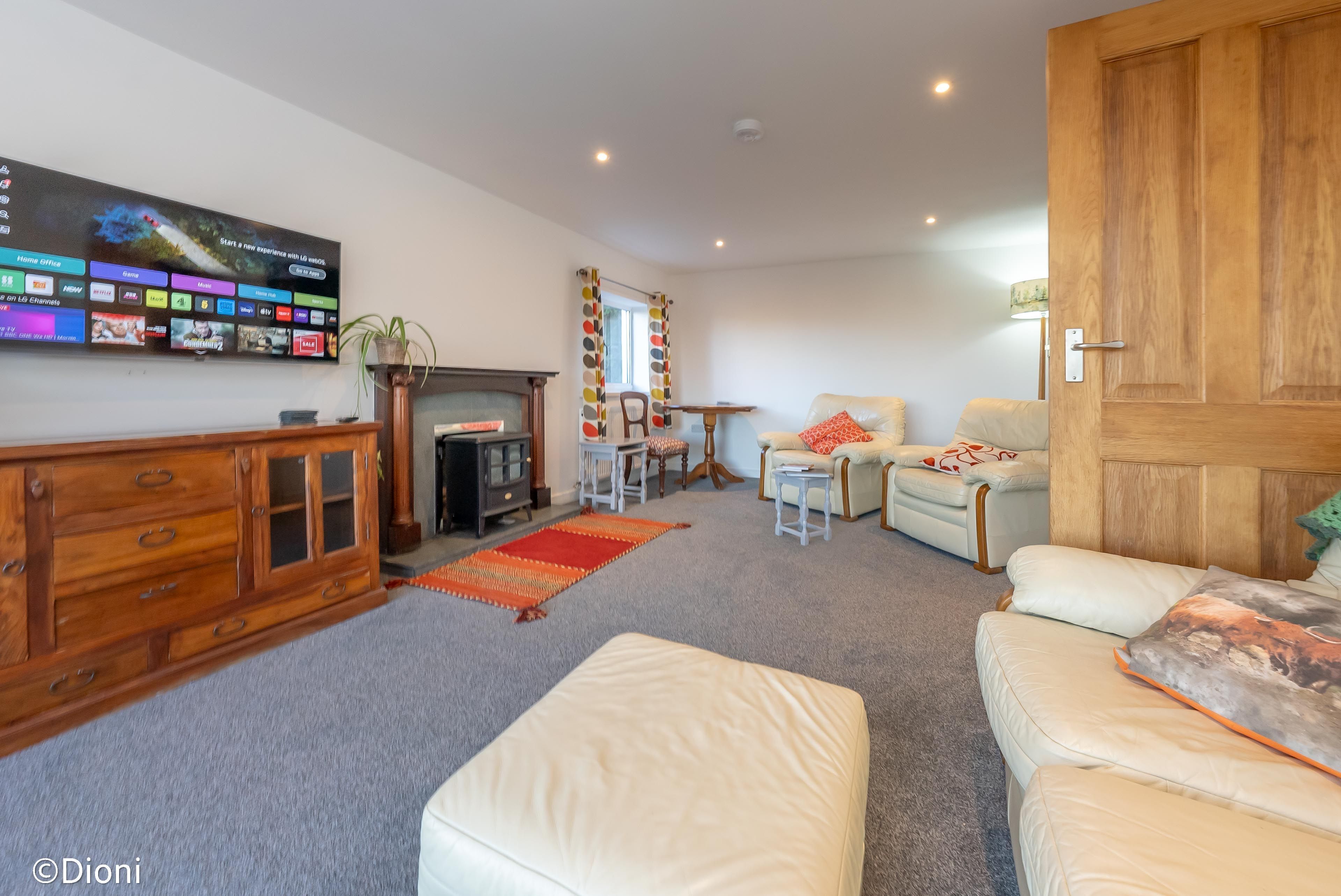 Een woonkamer met een flatscreen televisie, een houten kast, een open haard, een bank en een deur.