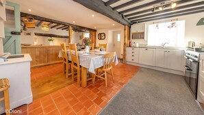 Una cocina con vigas de madera, una zona de comedor con una mesa dispuesta para cuatro personas y un piso de baldosas.