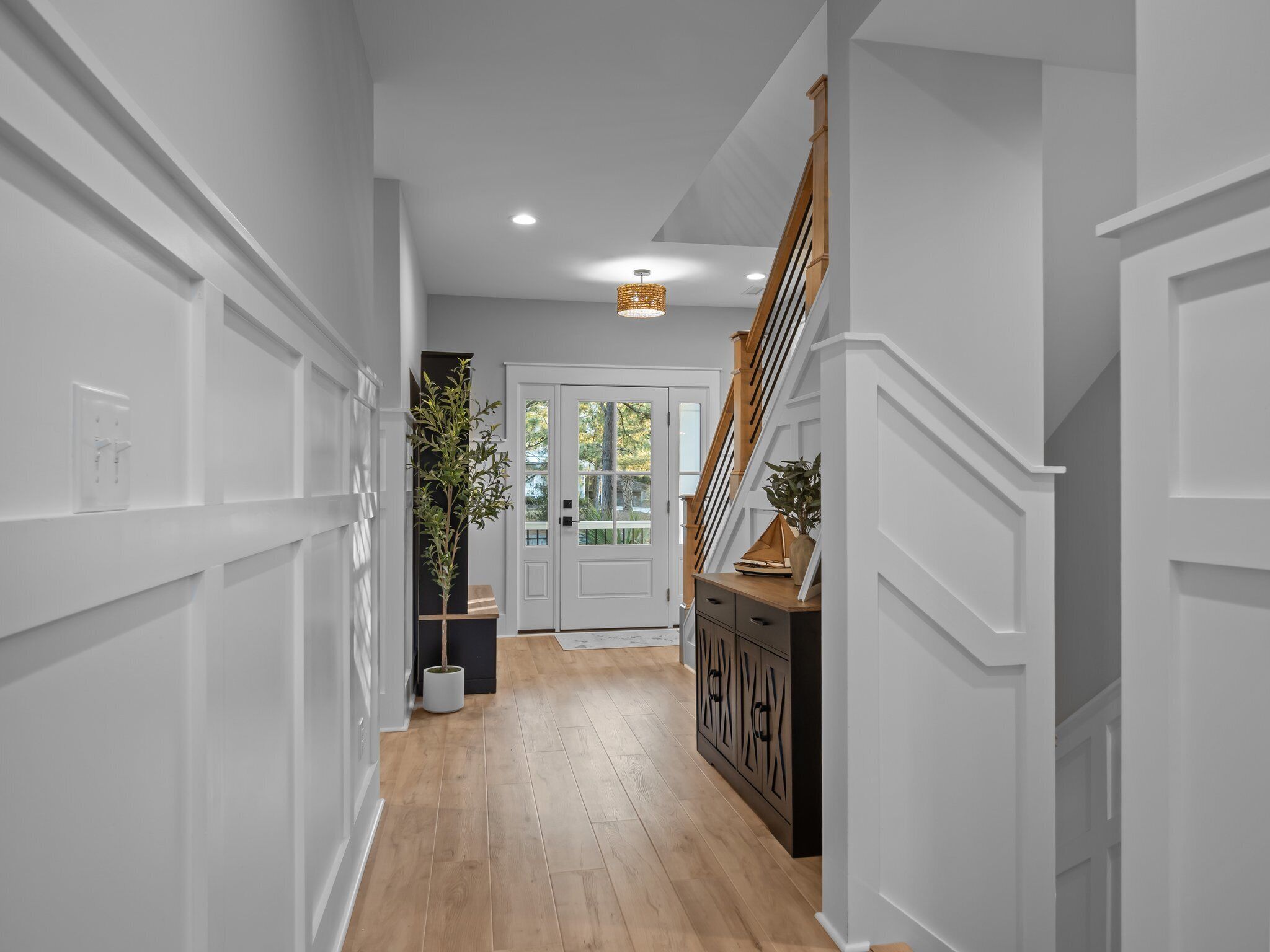 A hallway with wooden flooring, white walls, a staircase, and a door with glass panels.