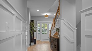 A hallway with wooden flooring, white walls, a staircase, and a door with glass panels. - Private Pool + Hot Tub | New 5BR w/ Golf Cart – Steps to Beach (Emerald Isle)