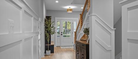 A hallway with wooden flooring, white walls, a staircase, and a door with glass panels.