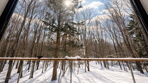 Quarto com uma grande janela que oferece vista para uma floresta nevada e um céu limpo.