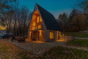 Une maison moderne avec un toit à forte pente, de grandes fenêtres et une terrasse pavée de pierres.