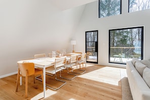 A modern interior with a dining area, a sofa, and large windows offering a view of the outdoors. - Modern A-Frame Catskills, Hot Tub & Fireplace (Napanoch)