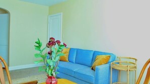 Un salón con un sofá azul, un jarrón rojo con flores y una mesa amarilla.