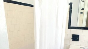 Un baño con bañera, un lavamanos blanco, armarios de madera y pared con azulejos.