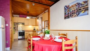 A dining area with a red tablecloth, wooden chairs, and a kitchen in the background. - Gîte Le Nain Rouge – 18th-Century Alsatian House in Kaysersberg (Kaysersberg Vignoble)