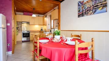 A dining area with a red tablecloth, wooden chairs, and a kitchen in the background.