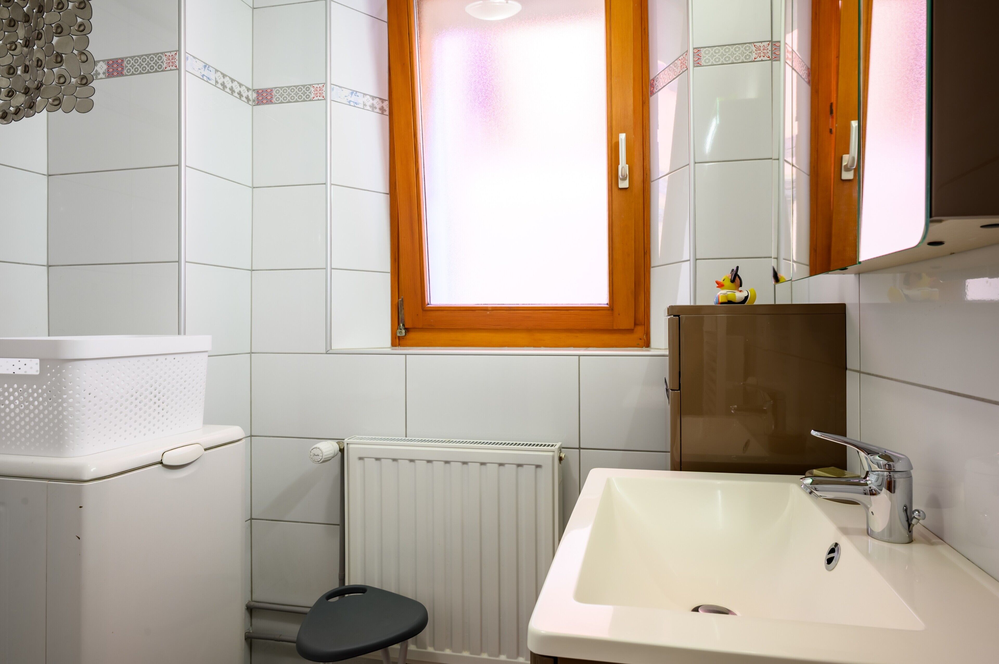 Een badkamer met een wit wastafel, toilet, radiator en raam met houten kader.