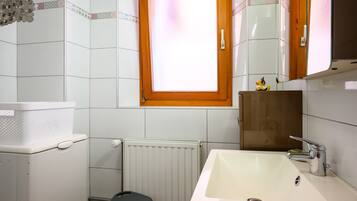Een badkamer met een wit wastafel, toilet, radiator en raam met houten kader.