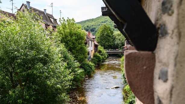 A narrow river with buildings on one side and a bridge in the distance. - Gîte Le Nain Rouge – 18th-Century Alsatian House in Kaysersberg (Kaysersberg Vignoble)