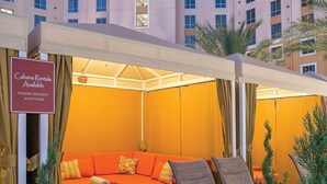 A cozy outdoor seating area with a red sofa and lounge chairs, a sign indicating Cabana Rentals, and a palm tree in the foreground. - Family Friendly Condo - No Resort fees! (Las Vegas)