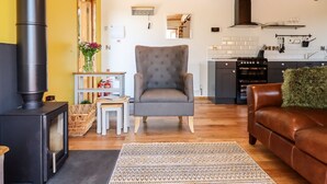Un salon chaleureux avec une cheminée, un fauteuil confortable, un canapé et, au fond, une cuisine.