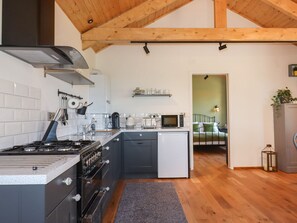 A modern kitchen with a stove, oven, microwave, and sink. There is a small island with a sink and a refrigerator. The kitchen has wooden beams on the ceiling and white tiled walls. - Nelli Lodge at Mile End (Crediton)