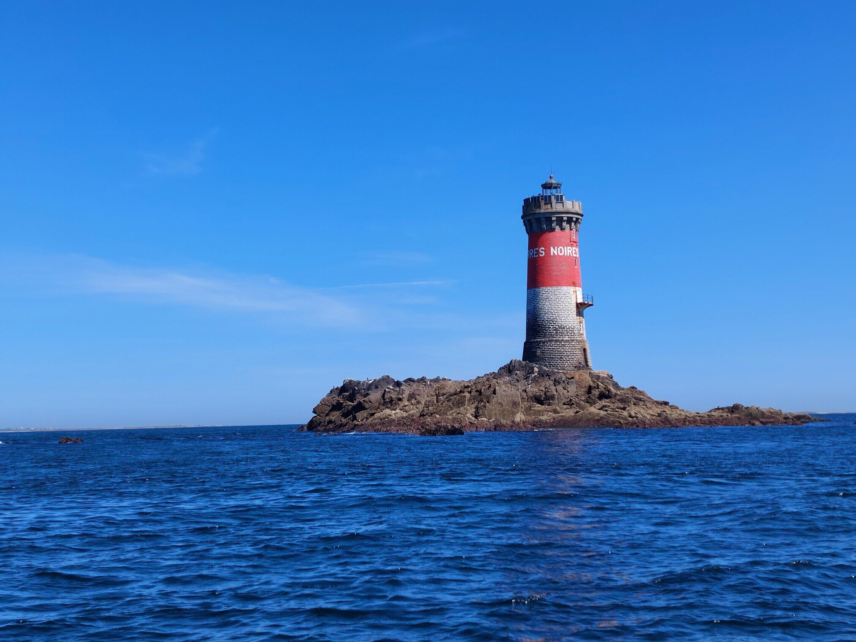 A lighthouse on a rocky island with clear blue water around it.