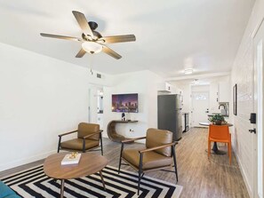 A modern living room with a ceiling fan, two leather chairs, a coffee table, a TV, and a kitchen area in the background. - Dawn-In Old Town-Walk to Entertainment District (Scottsdale)