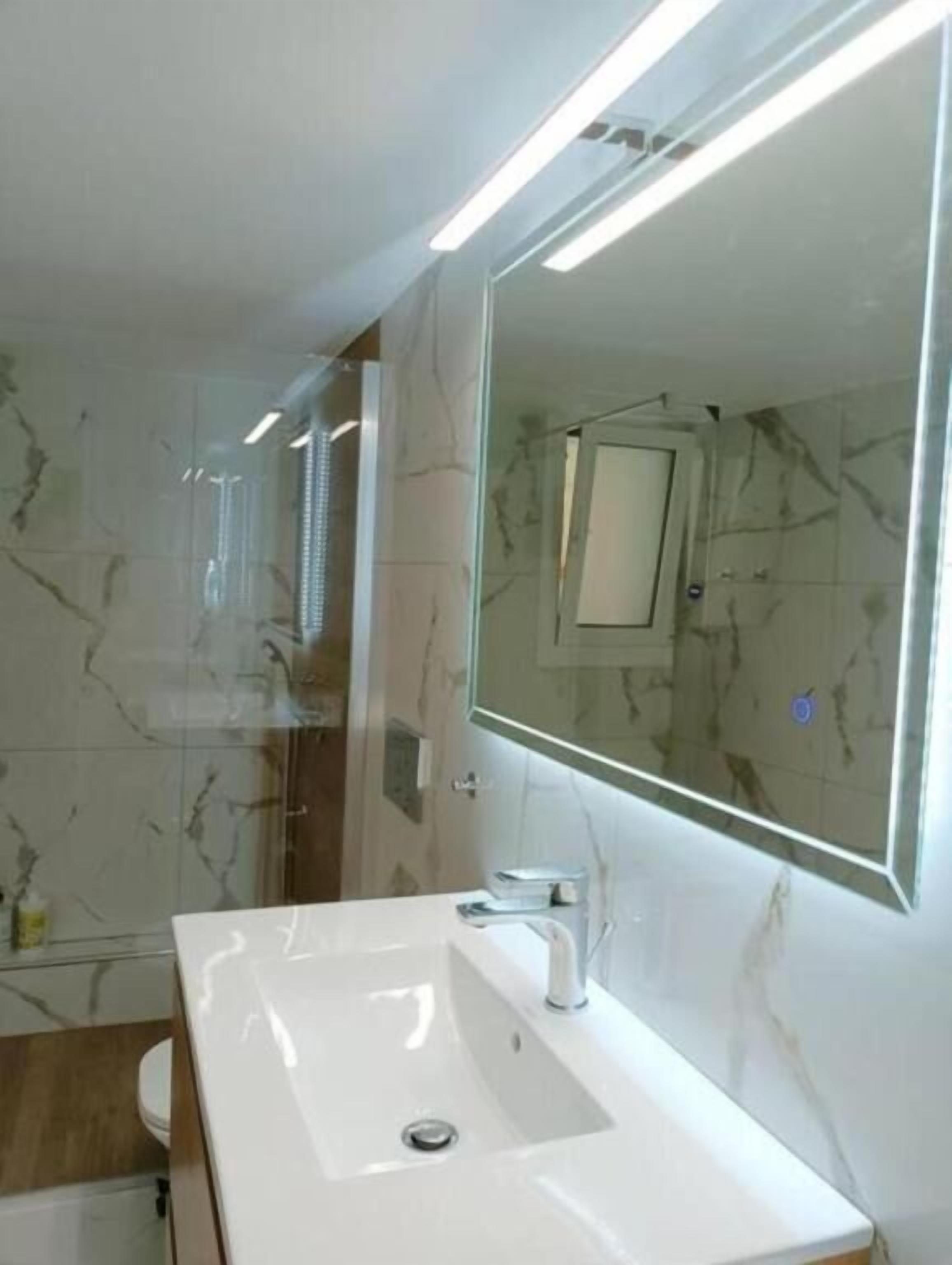 Une salle de bain moderne avec un grand miroir, un lavabo blanc et des murs en marbre.