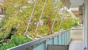 A balcony with two chairs and a table, overlooking a garden with trees and a building in the background. - Marousi Serene Suite (Marousi)