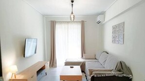A modern living room with a sofa, a coffee table, a TV, and a wall-mounted air conditioner. - Marousi Serene Suite (Marousi)