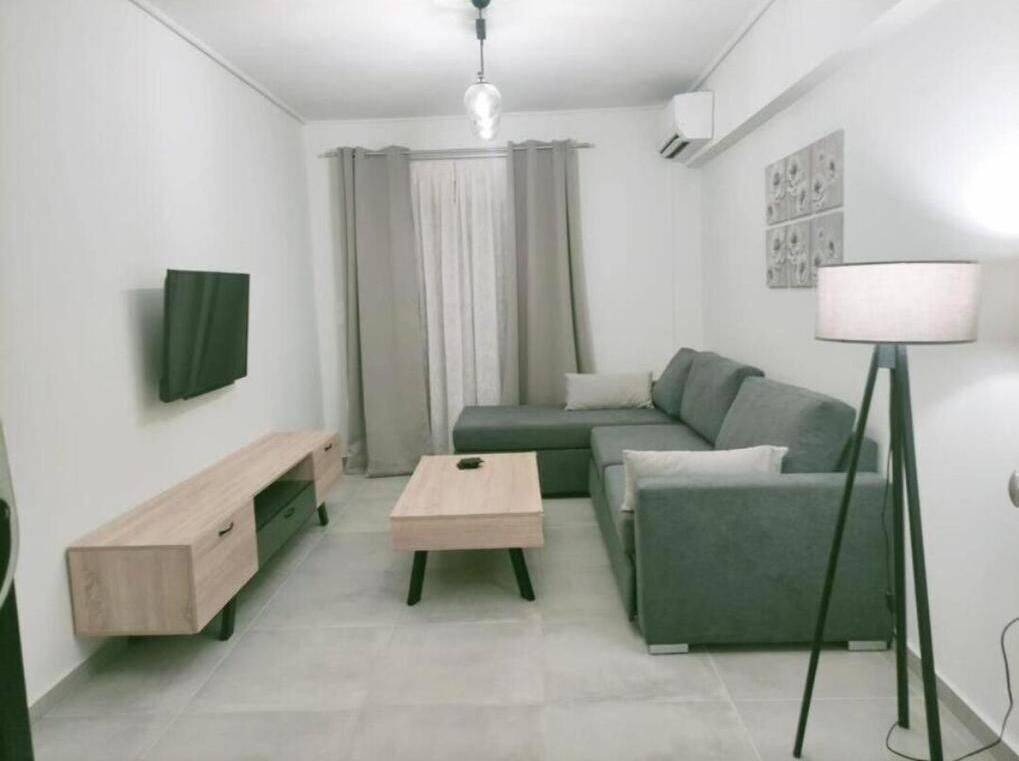 A modern living room with a grey sofa, a wooden coffee table, a TV mounted on the wall, and a floor lamp.