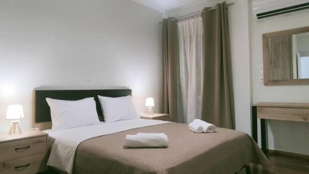 A neatly made bed with a headboard, a bedside table with a lamp, and a mirror on the wall. - Marousi Serene Suite (Marousi)