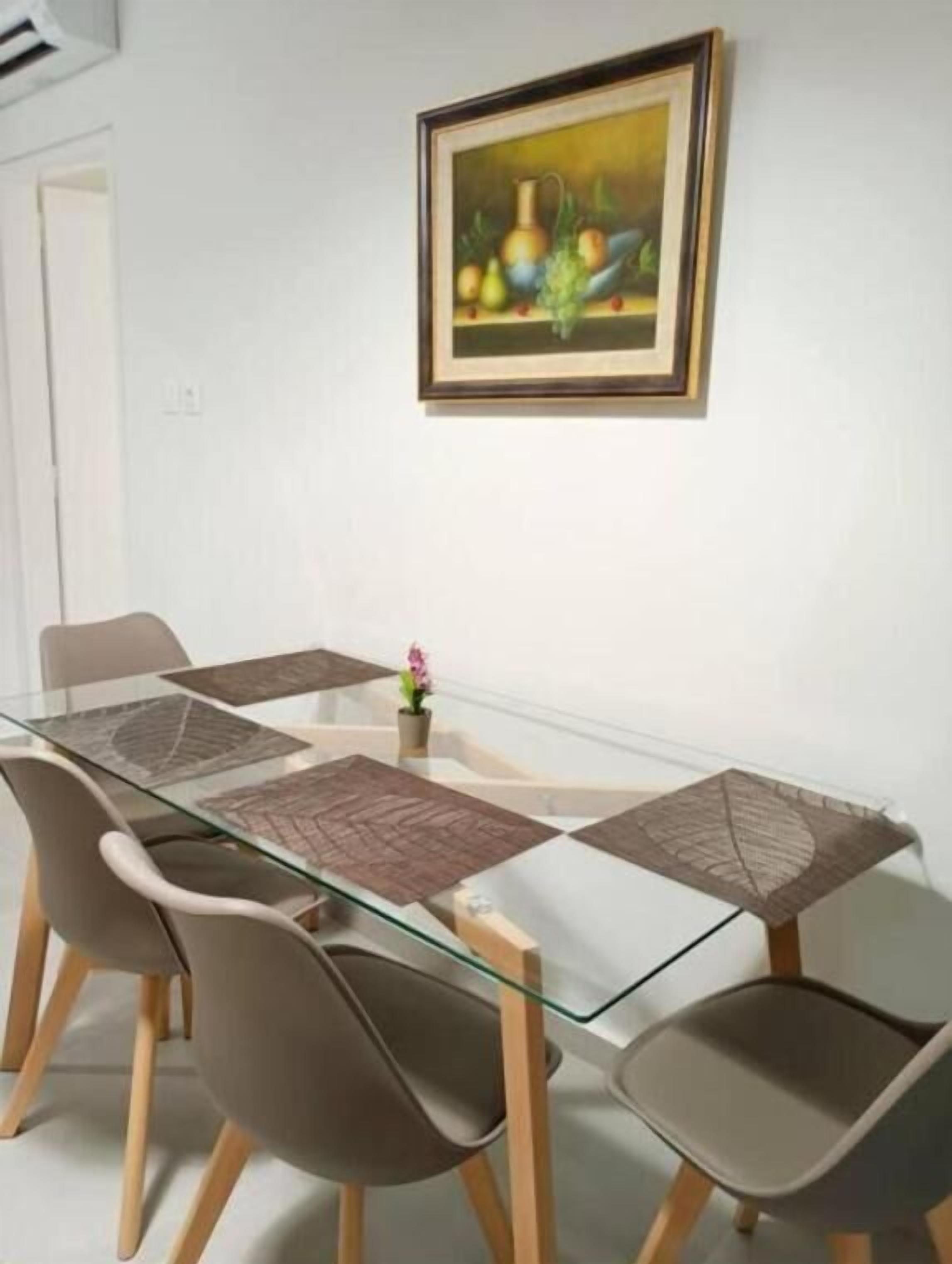 A modern dining area with a glass table, four chairs, and a framed painting on the wall.