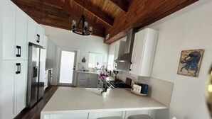 A modern kitchen with white cabinets, a central island with seating, a stainless steel refrigerator, and a wooden ceiling. - Escape & Relax in the heart of Key Largo, Florida (Key Largo)