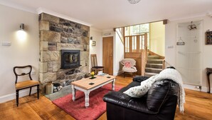 Ein gemütliches Wohnzimmer mit Kamin aus Stein, einem Holztisch, einer Ledersofa und einer Treppe, die zu einer weiteren Ebene führt.