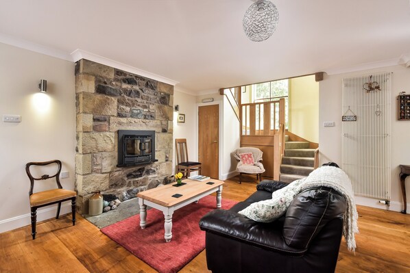 A cozy living room with a stone fireplace, a wooden coffee table, a leather sofa, and a staircase leading to another level. - A large spacious 3 bedroomed house in farmyard courtyard. (Perth)