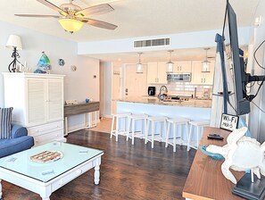 Un salon moderne avec une table basse en verre, un canapé, un meuble blanc et un coin cuisine avec un bar.