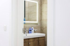 A bathroom with a white sink, a mirror, and toiletries on the countertop.