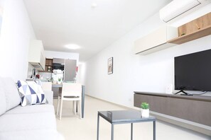 A modern living room with a sofa, a small table, a TV, and a kitchen in the background. - Central Sliema Stay | Sea View -Steps to Promenade (Sliema)