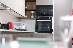 A modern kitchen with a built-in microwave, oven, and a wooden shelf above the oven.