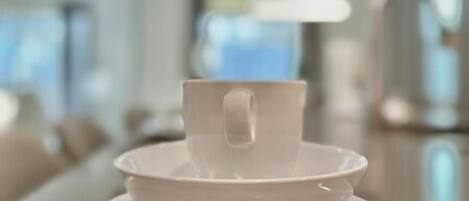 Een witte kop en schotel op een tafel in een moderne, goed verlichte kamer met een neutrale kleurenpalet.