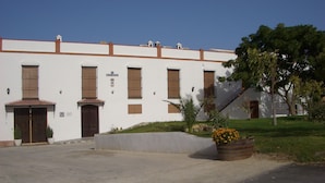 Un edificio blanco con varias ventanas y puertas, un letrero que dice 'Patrimonial', y una pequeña área de jardín con un macetero de flores amarillas.