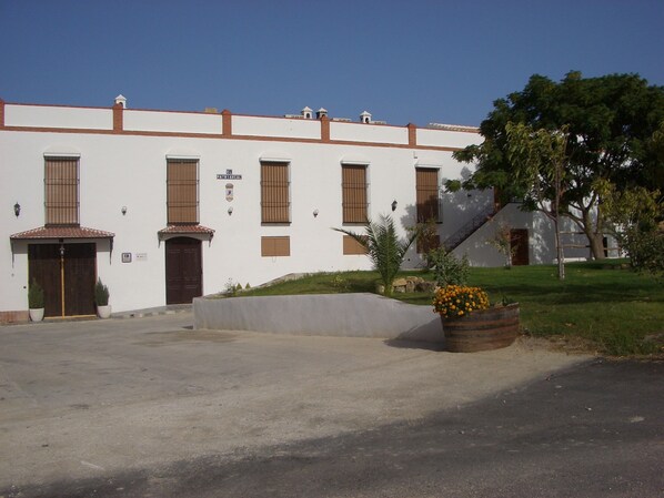 A white building with multiple windows and doors, a sign reading 'Patrimonial,' and a small garden area with a planter of yellow flowers. - Traditional Andalusian Mansion, Cordoba (Moriles)