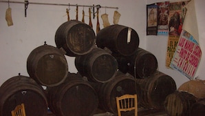 Una habitación con varios barriles de madera apilados contra la pared, una silla de madera al frente y un cartel en la pared.
