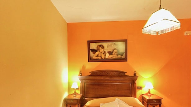 Habitación de hotel con una cama, dos mesitas de noche con lámparas, un cabecero de madera y un cuadro sobre la cama.